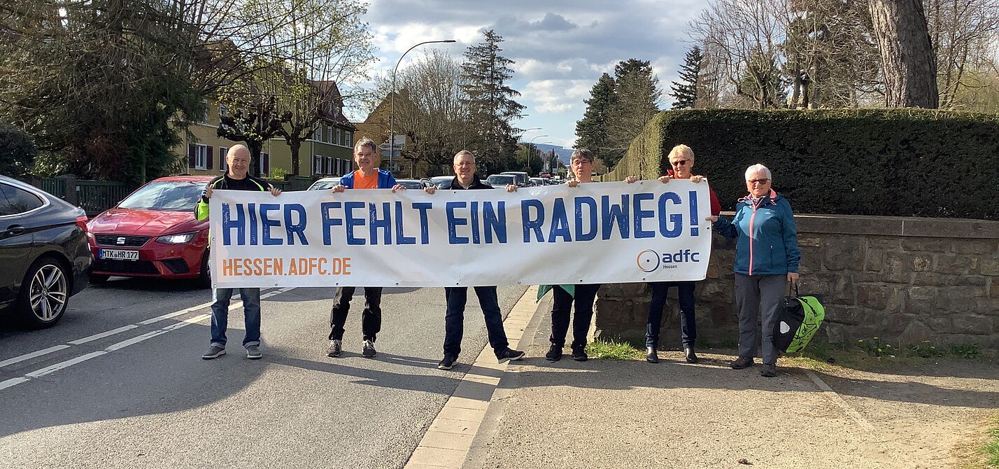 Personengruppe hält Banner hoch "Hier fehlt ein RAdweg"