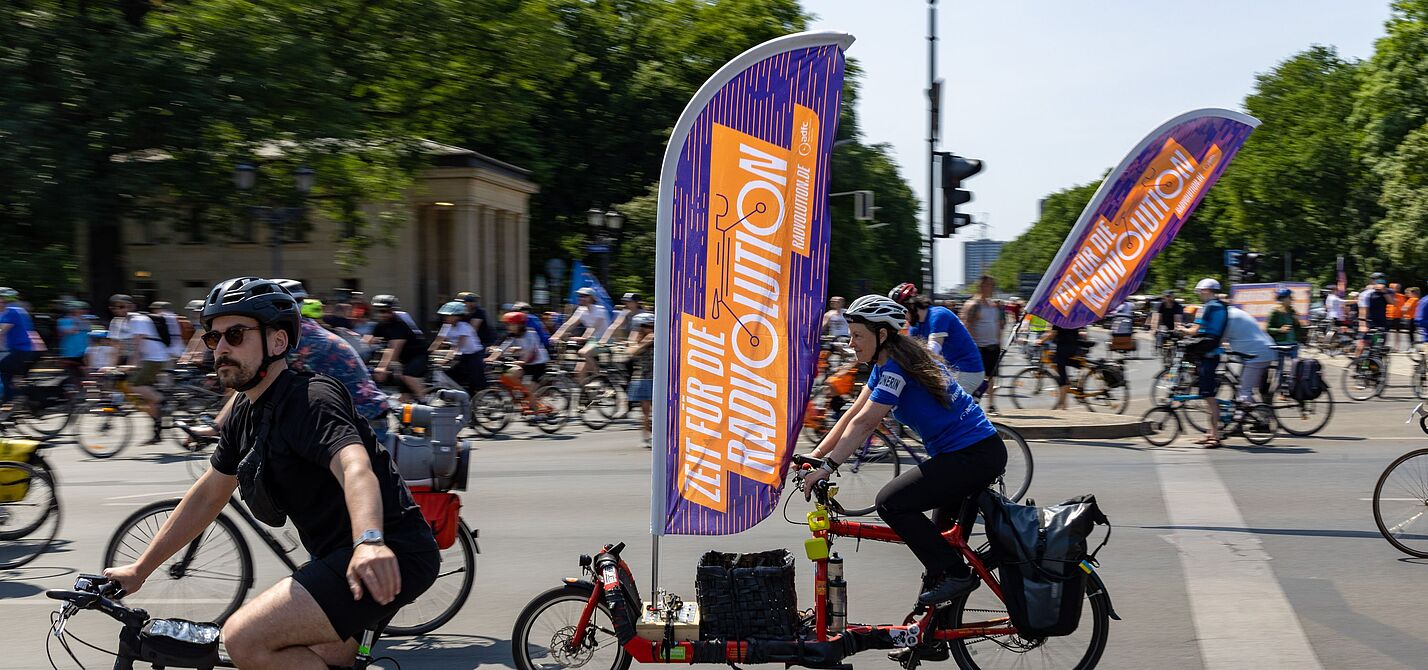 Viele Menschen auf Fahrrädern. An einem Rad befindet sich eine große Fahne mit dem Wort "Radvolution" darauf.